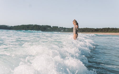 Side view of woman in swimsuit standing in foamy waves of ocean in tropical area in sunny day