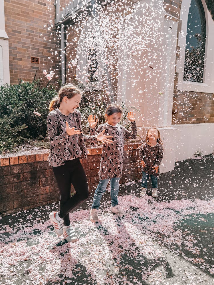 Happy Children Playing With Pink Feathers In Street Near Building