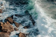 阳光明媚的夏日里，波浪般的泡沫黑色海洋溅在海岸上潮湿的大岩石上