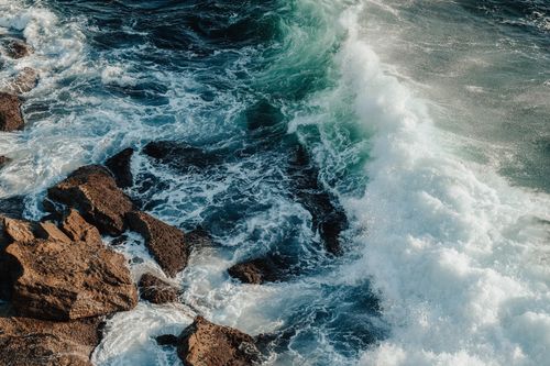 Free Wavy foamy dark ocean splashing on big wet rocky boulders on coast in sunny summer day Stock Photo