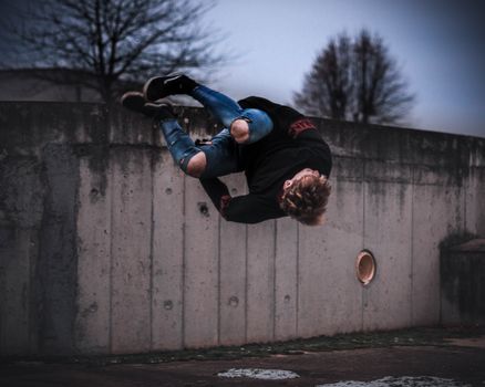 A skilled parkour athlete performing a midair side flip against a concrete wall during the daytime.