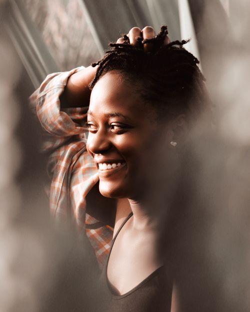 Free Close-up portrait of a smiling black woman with dreadlocks and hand on head, exuding happiness. Stock Photo