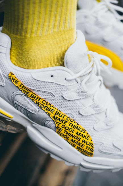 Close-up of white sports shoe with yellow accents and text detail, paired with yellow socks.