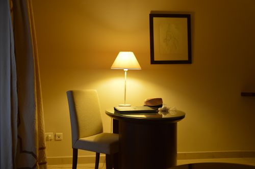 Free Warmly lit room with a chair, table, and a soft glowing lamp creating a cozy ambience. Stock Photo