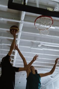 Exciting indoor basketball game with female athletes reaching for the hoop.