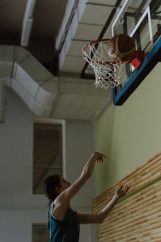 Female basketball player making a shot indoors, showcasing sportsmanship and focus.