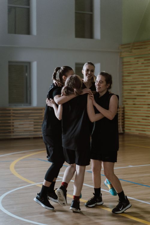 Free Four young women basketball players hugging and celebrating victory indoors. Stock Photo