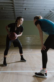 Two female athletes face-off on an indoor basketball court, showcasing competitive spirit.