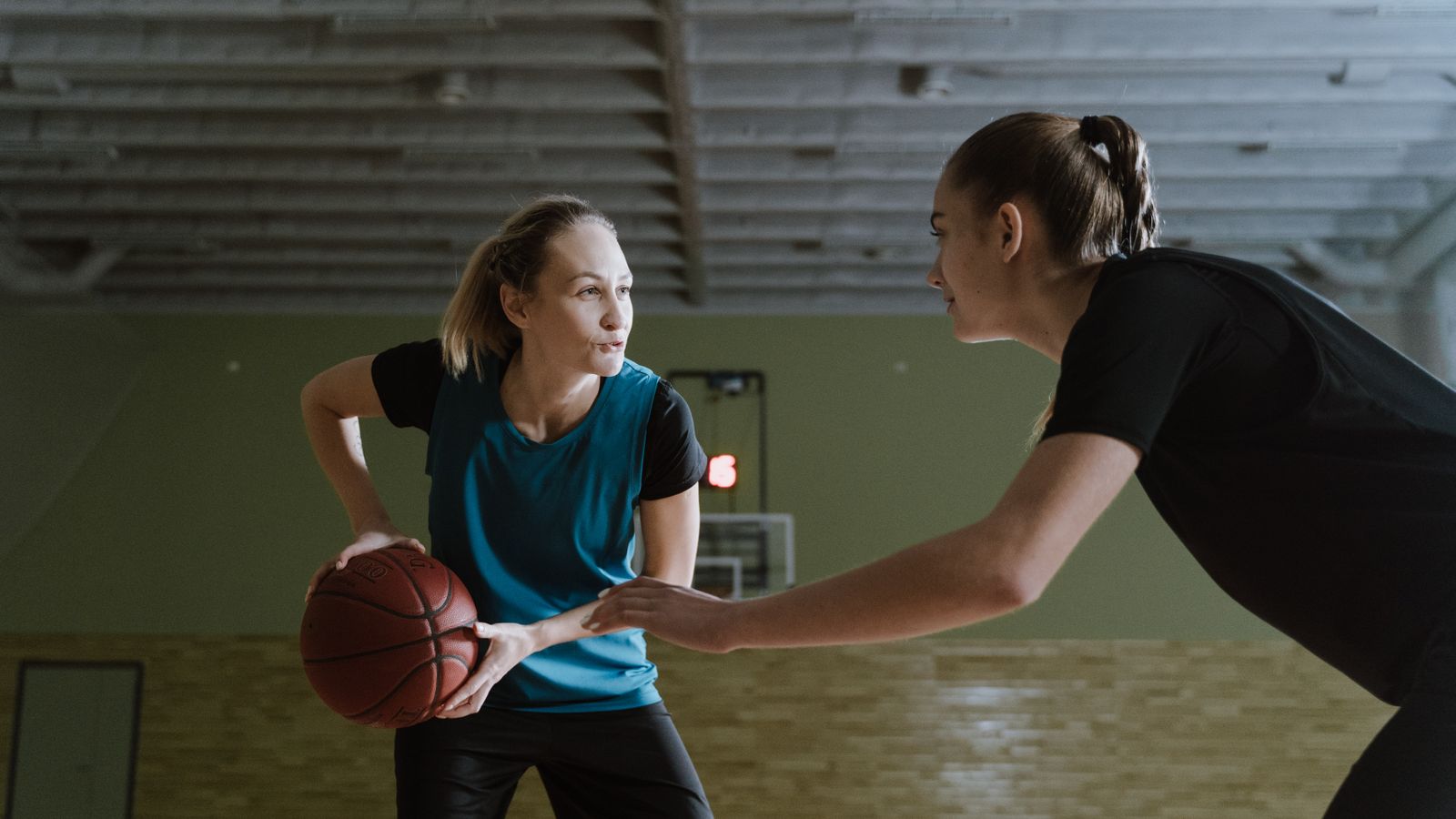 Two women athletes engage in a competitive basketball game indoors.