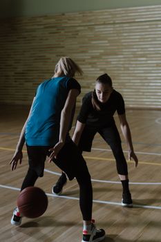 Two women playing an intense game of basketball indoors, focused and competitive.