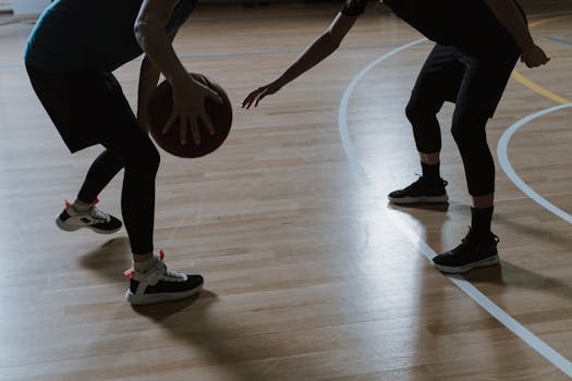 Silhouette of two players engaged in a basketball match on an indoor court.