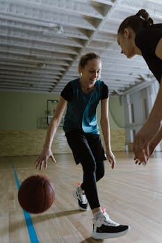 Two women actively playing basketball indoors on a court, showcasing energy and teamwork.