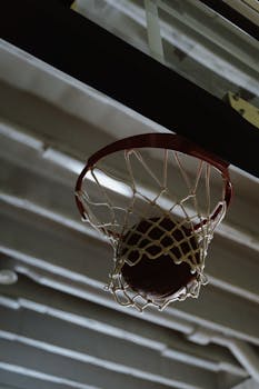 Close-up shot of a basketball in a hoop inside a gymnasium.