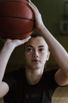 A young sportswoman intensely focuses on shooting a basketball indoors.