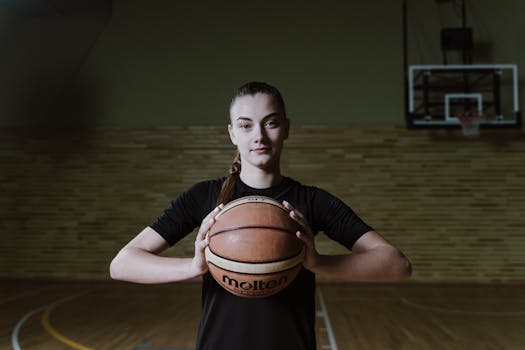Young woman holding basketball confidently on an indoor court, ready for action.