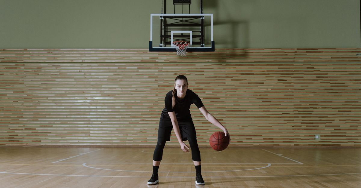 Young athlete practicing basketball drills in a dimly lit gym at dawn