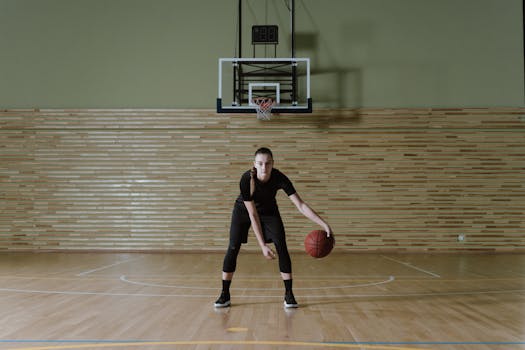 Focused young woman dribbling basketball in indoor court, embodying determination and athleticism.