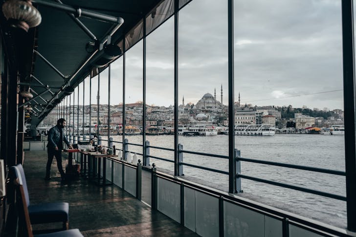 Full body of male tourist standing near table on ship deck floating on rippling waterway in Istanbul