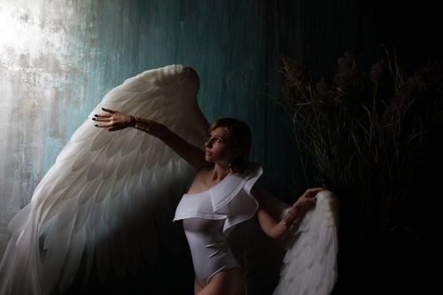 Free Side view of young woman in white bodysuit with decorative wings looking up against rugged wall Stock Photo