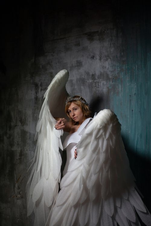 Free Young gentle female in crown with white decorative wings looking away against rough wall Stock Photo