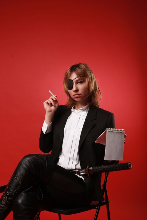 Free Young confident female in pirate eye patch with notebook looking at camera while sitting with crossed legs on chair Stock Photo