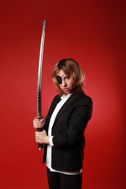 Young woman in formal wear and pirate eye patch with Japanese sword looking at camera