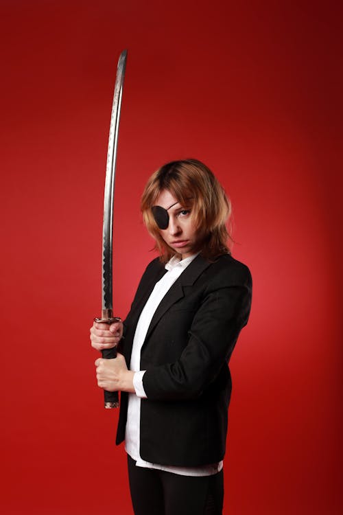 Free Young woman in formal wear and pirate eye patch with Japanese sword looking at camera Stock Photo