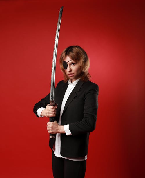 Free Confident young woman in formal outfit with Japanese sword looking at camera on red background Stock Photo