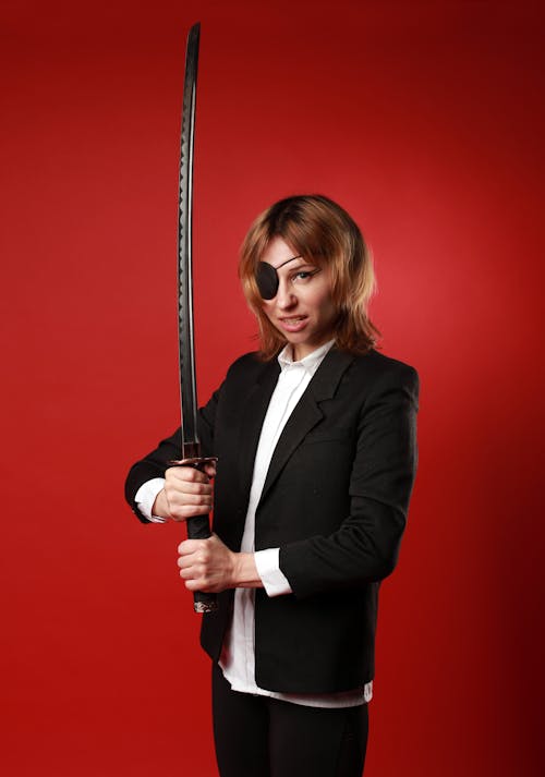 Free Young strong female in stylish wear and pirate eye patch with Japanese sword looking at camera Stock Photo