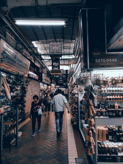 Free People shopping and walking through a vibrant indoor market aisle, packed with various shops and products. Stock Photo