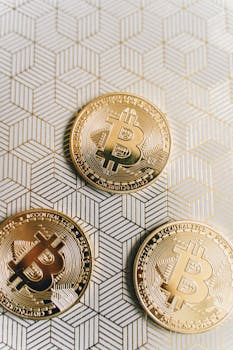 Close-up of three shiny bitcoin gold coins on a geometric pattern background, symbolizing cryptocurrency.