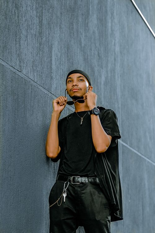 Free Stylish young man in black outfit posing against a gray wall, exuding confidence and fashion-forward style. Stock Photo