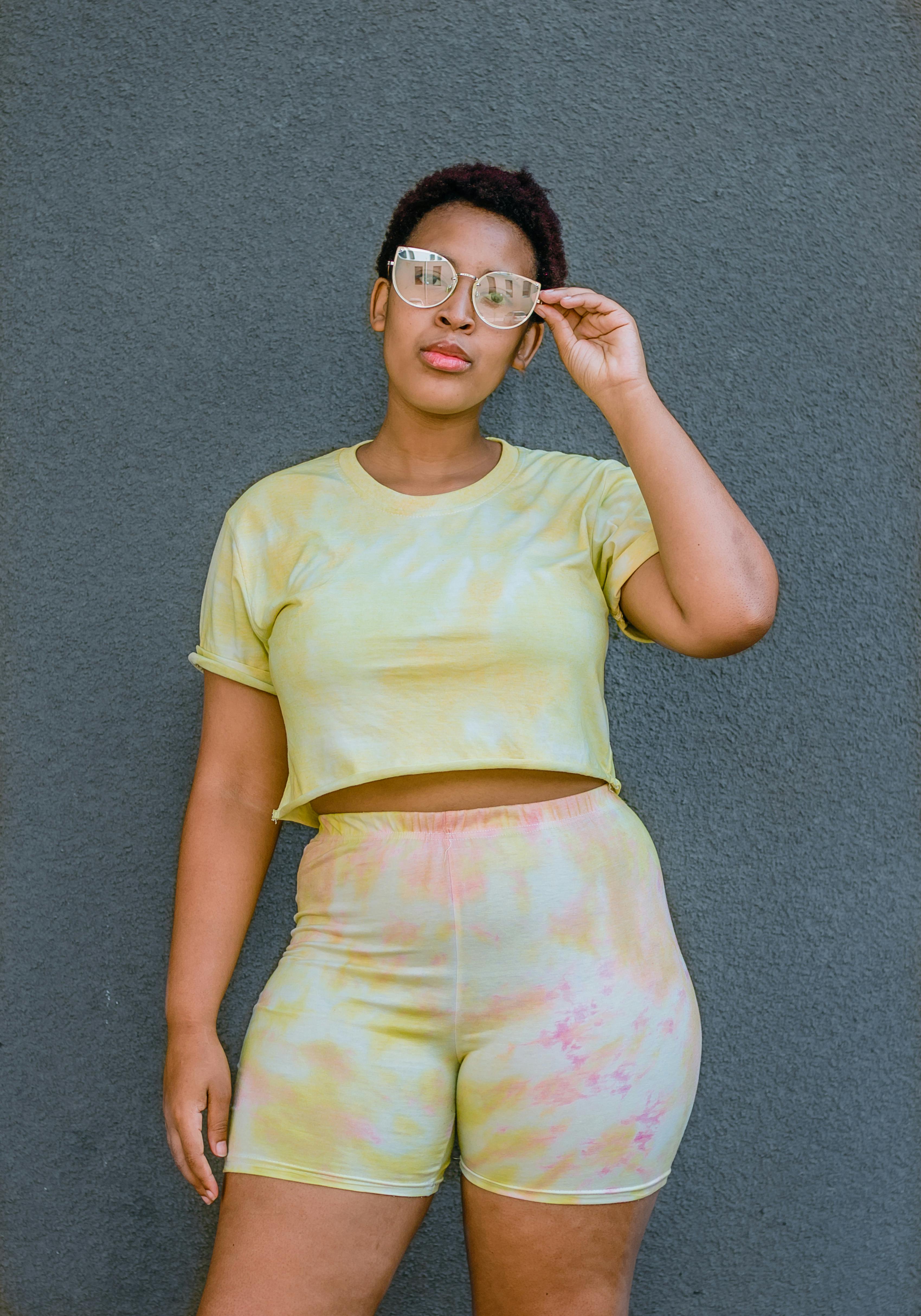 Confident young Black woman posing in trendy tie-dye sportswear against a gray wall.