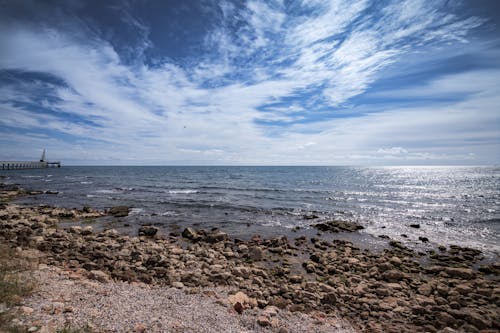 Picturesque sea with stony coast under cloudy sky