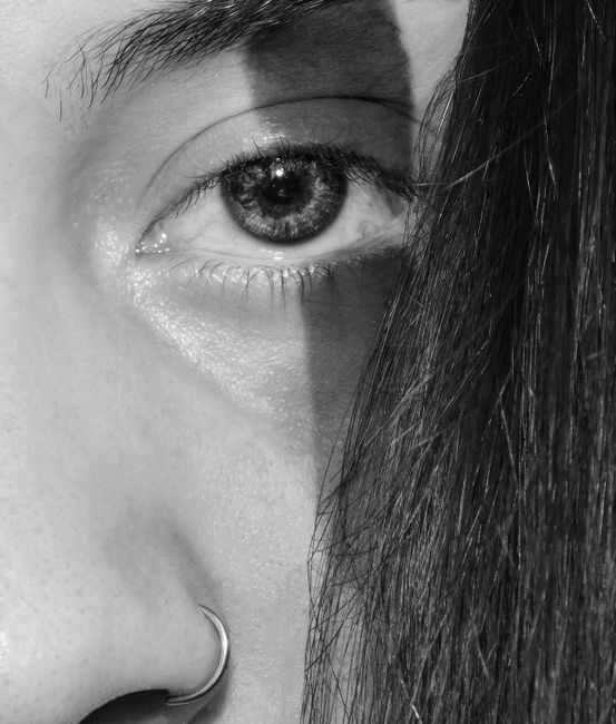 Artistic close-up grayscale image of an eye with a nose ring, creating a dramatic effect.