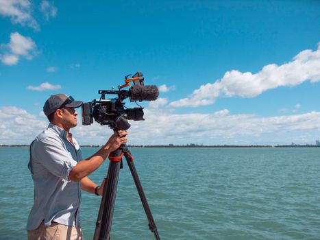 Man filming with a camera against the Miami ocean view on a sunny day.