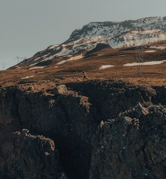 A lonely figure walks on a vast, rugged mountain landscape under a clear sky.