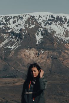 A woman in a windbreaker stands before snow-capped mountains, capturing an adventure vibe.