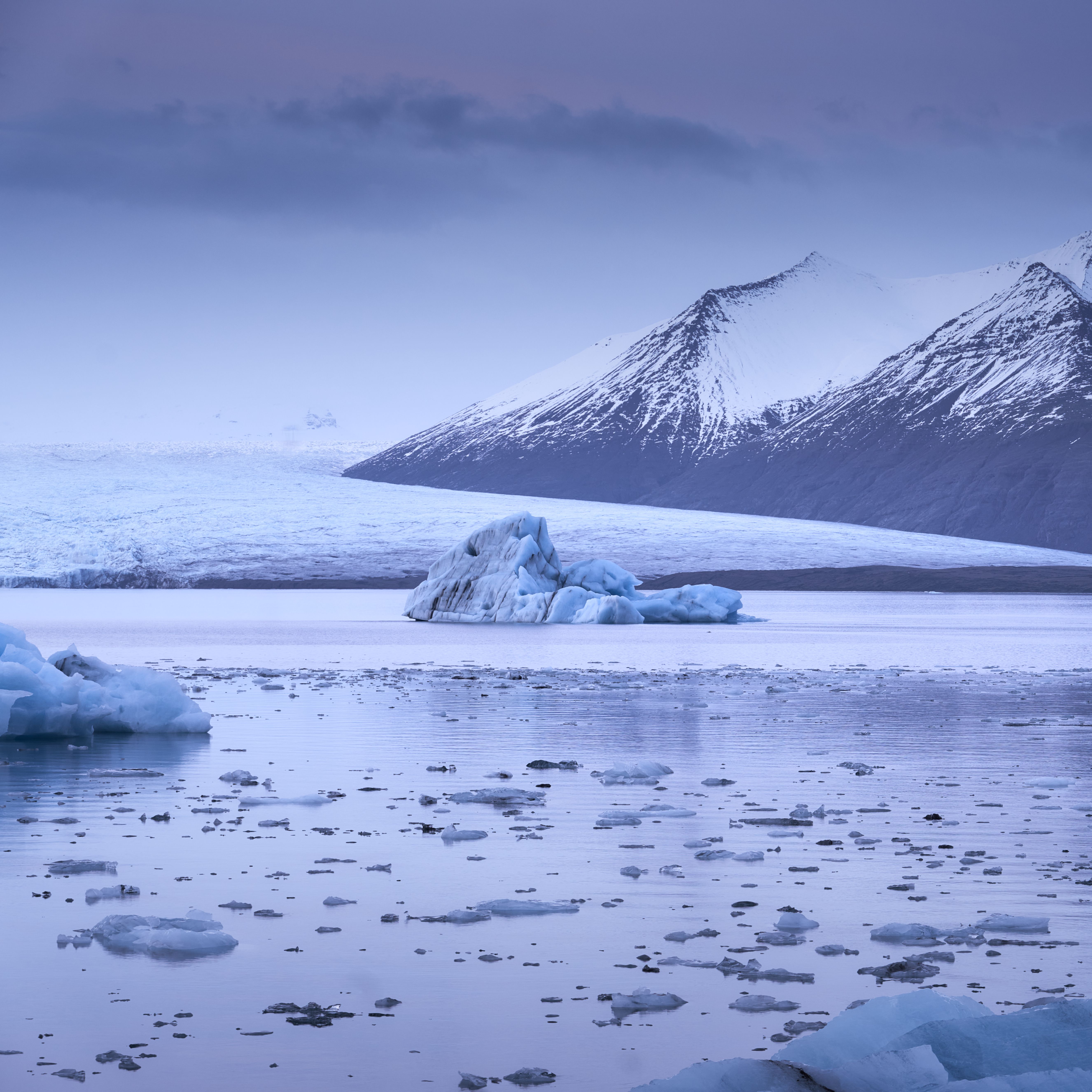 Serene view of snow-covered mountains and icebergs in a tranquil Icelandic landscape.