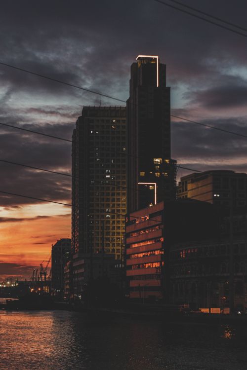 Free Evening view of Manila's skyline with lit high-rises against a dramatic sunset over the water. Stock Photo