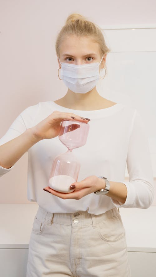 Woman in Facemask Holding Hourglass