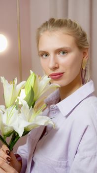 Smiling woman with white lilies in a cozy indoor setting, showcasing elegant simplicity.