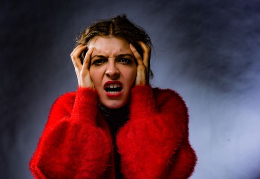 A woman in a red sweater expressing anger and frustration in a studio portrait.