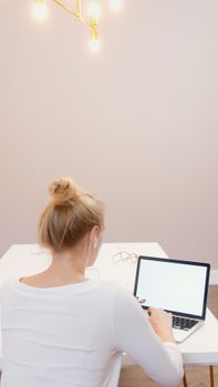 A woman with a hair bun working on a laptop at a simple home office desk.