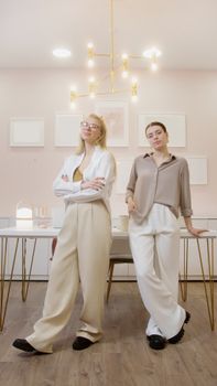 Two stylish women posing confidently in a modern interior setting, exuding elegance and poise.
