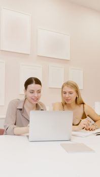 Two women working together on a laptop in a modern office setting.