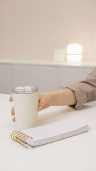 A minimalist workspace with a hand holding a cup, notepad on the table.