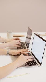 Two people typing on laptops in an office setting, emphasizing teamwork and productivity.
