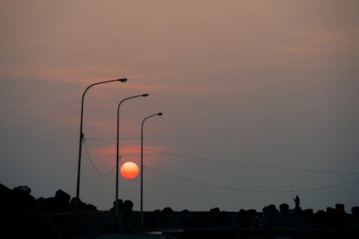 Silhouette of street lamps and a fisherman at sunset in Taiwan, creating a serene scene.