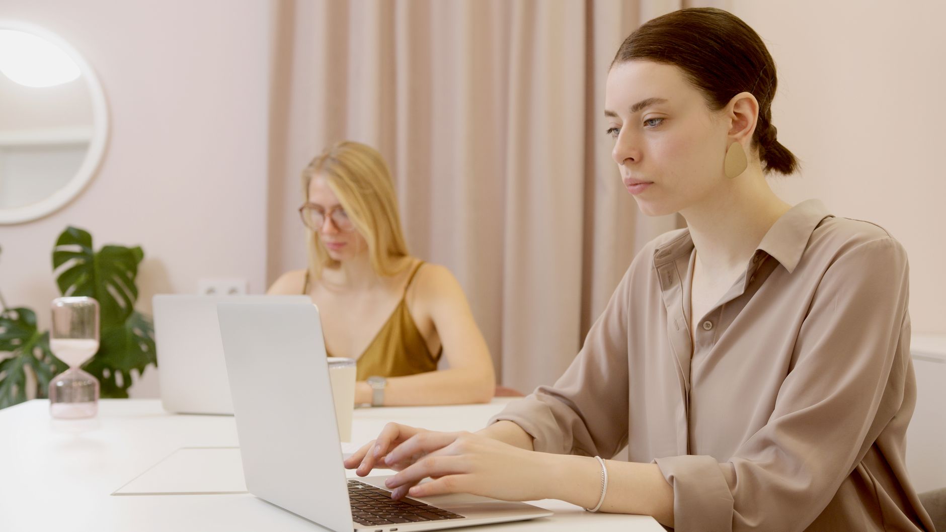 Two women concentrating on their laptops in a well-lit office setting, creating a focused work environment.
